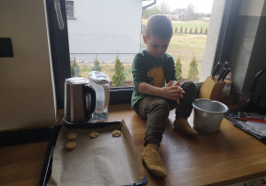 dziecko wyrabia ciasto siedząc na blacie kuchennym pod oknem